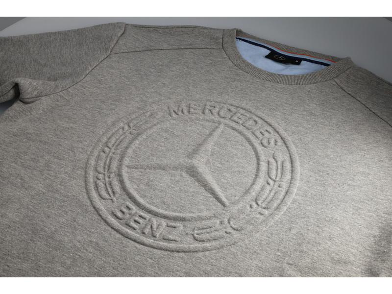 Nahaufnahme des geprägten Mercedes-Sterns in 3D-Optik auf der Vorderseite des grauen Sweatshirts.