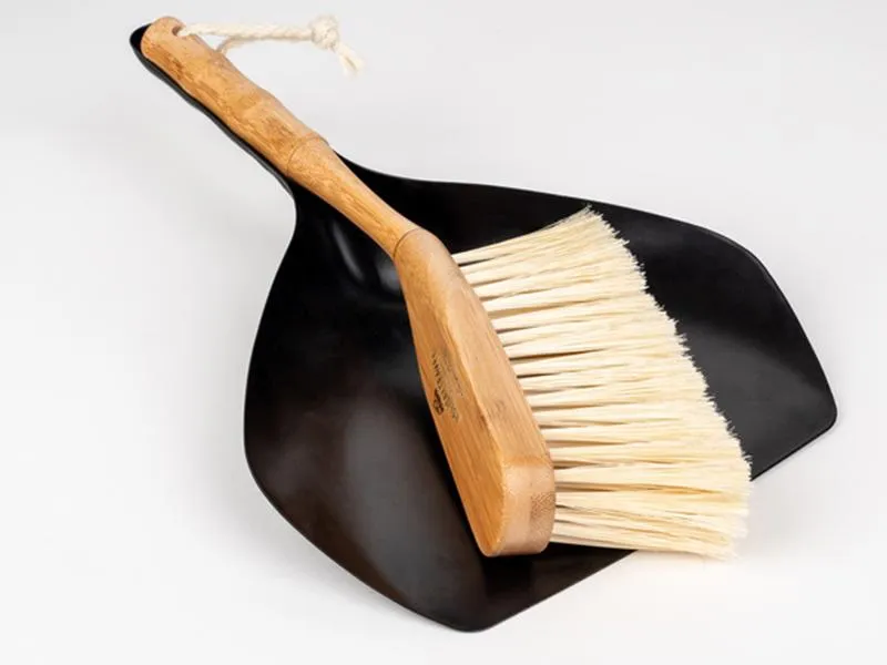 Abgebildet ist das Camping Handfeger- und Kehrschaufel-Set, bestehend aus einem Handfeger mit Bambusgriff und einer schwarzen Metall-Kehrschaufel. Ideal zur einfachen Reinigung von Campingplätzen und Outdoor-Bereichen