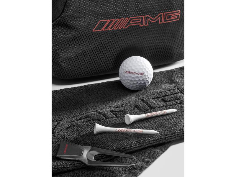 Nahaufnahme des AMG Golf-Geschenksets: schwarze Tasche mit rotem AMG-Schriftzug, Golfball und weiße Tees auf einem Schlägerhandtuch.