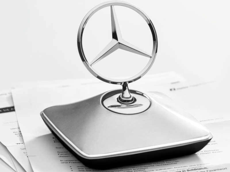 Briefbeschwerer im Mercedes-Benz Design mit ikonischem Kühlerhaubenstern, auf einem Schreibtisch mit Dokumenten platziert. Elegantes Accessoire in silvershadow/chrom/schwarz.