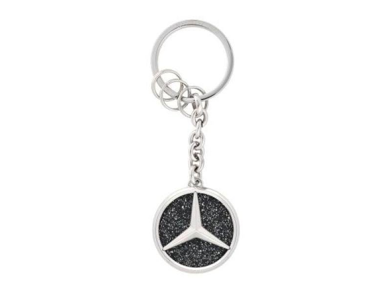 Mercedes-Benz Schlüsselanhänger Saint Tropez in Silber mit schwarzem Kristallglas. Der Anhänger zeigt das ikonische Mercedes-Stern-Logo und verfügt über einen stabilen Ring mit zusätzlichen Minispaltringen für einfaches Anbringen von Schlüsseln.